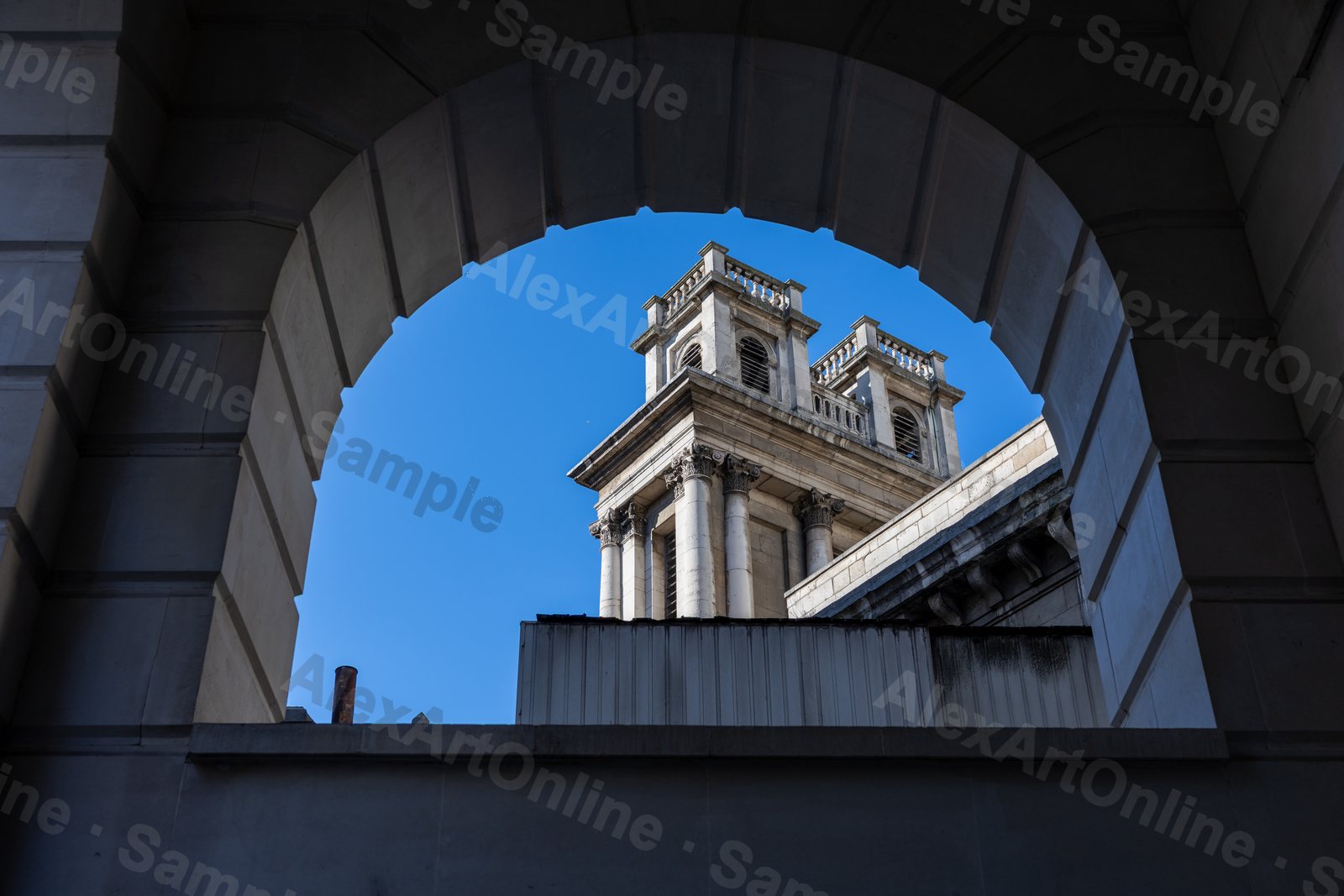A white stone tower framed by a dark archway and blue sky